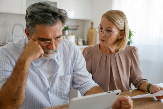 Couple discussing financial problems at home with bills and tablet