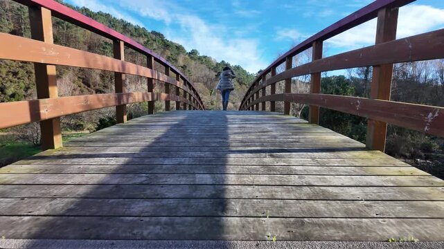 Low angle of person in rubber wellington boots walking across a wooden bridge in the forest