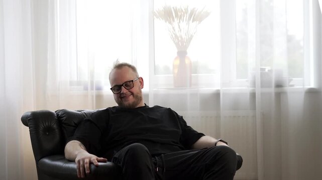 Smiling man sitting in armchair at home, nodding head in agreement with positive expression in cozy living room