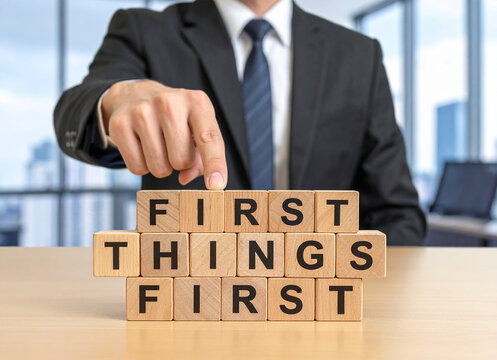 First things first - Geschäftsmann zeigt auf den Text "First things first"