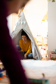 Young woman working on a laptop inside an Indian tent at home with family