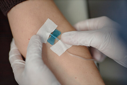 Doctor preparing IV drip infusion catheter on arm in hospital