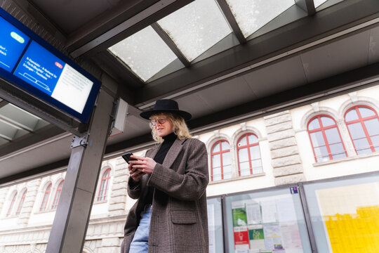 Young man waiting at train station using smartphone in urban setting