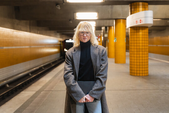 Young man waiting on urban subway platform holding laptop