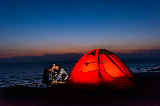 Couple messaging by tent at beach during summer evening