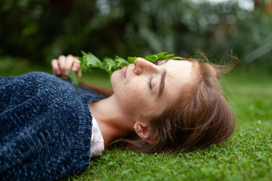 Freckled face person lying on grass with fern relaxing outdoors in summer