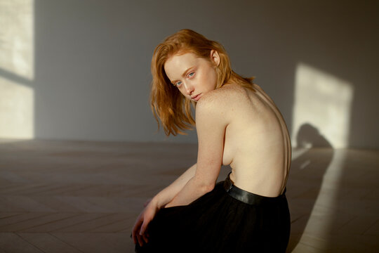 Red-haired model with freckles in sunlight posing with bare back