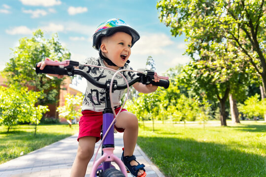 Portrait little cute adorable caucasian toddler boy in safety helmet enjoy having fun riding exercise bike in city park road yard garden forest. Child first bike. Kid outdoors sport summer activities