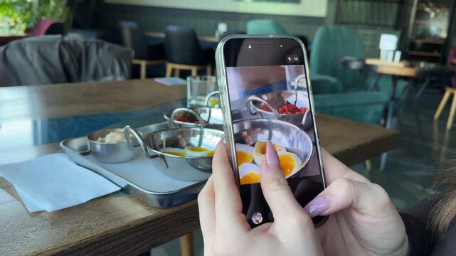 Female hands film a hotel breakfast with a mobile phone, focusing on soft-boiled eggs cut in half. shots and refocusing show a food blogging moment in a restaurant, capturing plated morning dishes.