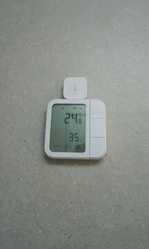 Smart home climate sensor with digital LCD display showing temperature and humidity.