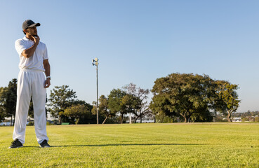 Indian man cricketer standing left on grass field, touching chin, wearing white uniform, copy space © wavebreak3