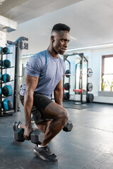 African American man performing weighted lunge holding hex dumbbells in gym in heather blue shirt © wavebreak3