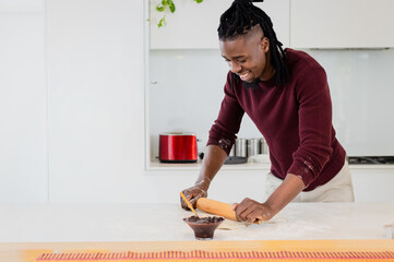 African American man wearing sweater rolling dough on kitchen island using rolling pin, copy space © wavebreak3