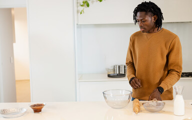African American man preparing batter at kitchen island with glass bowls, rolling pin, copy space © wavebreak3