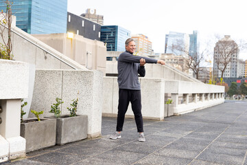 Man wearing athletic top, joggers stretching arm across chest steadying black sling bag on terrace © wavebreak3
