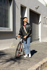 Man in his 20s checking while walking road bike with olive-green bag on sidewalk by building © wavebreak3