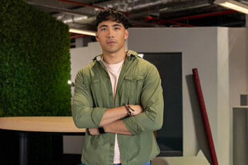 Asian man standing with arms crossed in office lounge near planted wall and table © wavebreak3