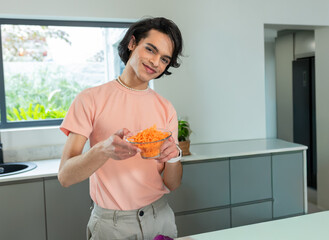 Male in pink shirt holding and presenting glass bowl of shredded carrots at kitchen counter © wavebreak3