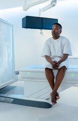 Control starting, patient sitting edge, gantry rotating, screens showing CT scans for diagnosis © wavebreak3