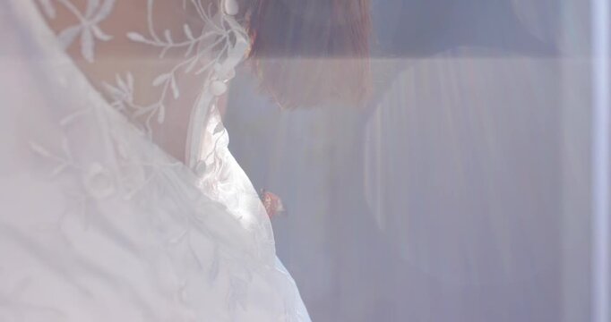 Adult woman in white lace dress tilting and adjusting corsage as camera settling near blue curtain