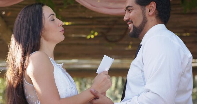 Diverse couple at pink drape arbor bride dress reading vows groom smiling hands camera pulling back