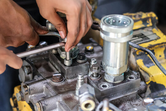 Close-up of a technician's hands using an L-key wrench to repair a heavy equipment hydraulic pump component in a mechanical workshop.