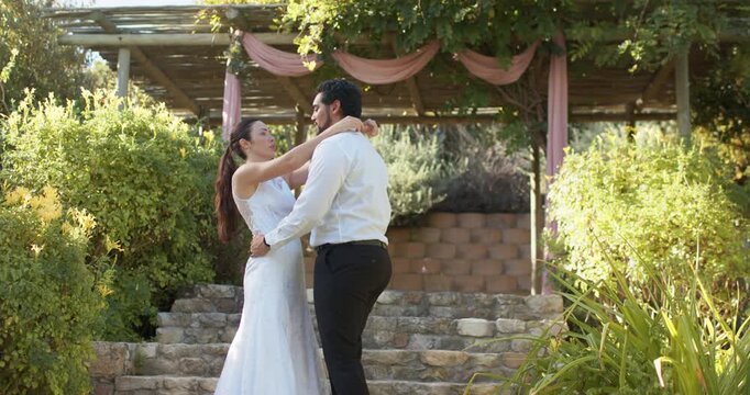 Bride and groom standing on stone steps under pergola, groom lifting hand, guiding twirl at wedding