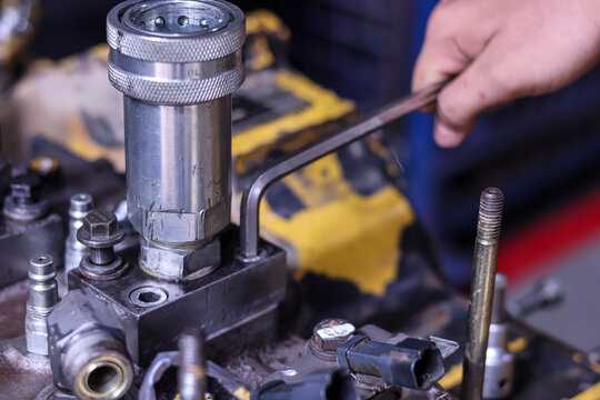 Close-up of a technician's hands using an L-key wrench to repair a heavy equipment hydraulic pump component in a mechanical workshop.