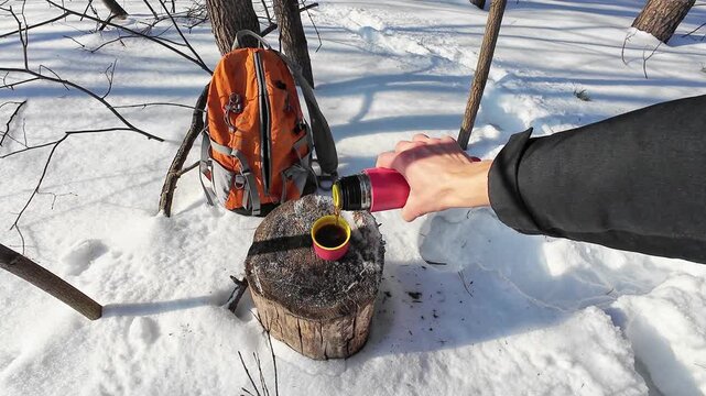 Outdoor Coffee Break Scene. Person Enjoys Hot Drink On Snowy Trail. Hiker At Rest Pours Warm Beverage Into Cup Amidst Snow. Individual In Woods Takes Moment To Sip Steaming Coffee On Snowy Day