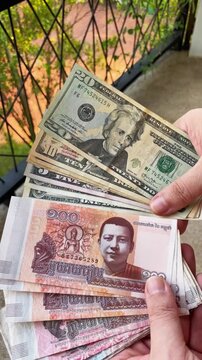 A close-up of a man's hands holding US dollars and Cambodian riels. Conceptual illustration of dual currency, cash payments, currency exchange, and everyday payments in Cambodia.