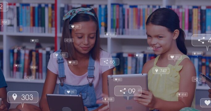 Reading 2 girls wearing denim overalls and yellow dress holding tablets in library showing UI icons