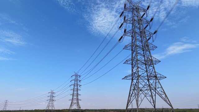 High voltage transmission towers across rural landscape under blue sky