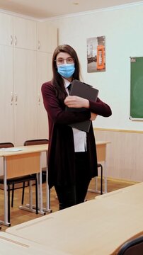 Remote teaching during lockdown: masked teacher with laptop in empty classroom