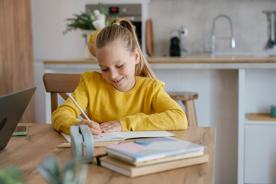 Child smiling while writing homework at home in modern kitchen