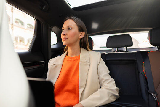 Businesswoman in blazer riding in car back seat during urban commute
