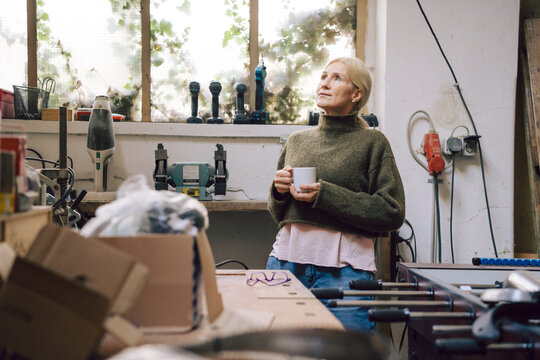 Mature woman taking a break in her workshop holding a cup