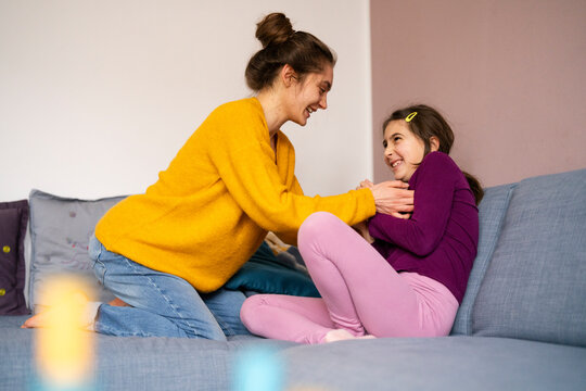 Big sister tickling little sister at home on the couch