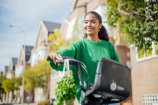 Smiling woman walking with bicycle and groceries on urban street
