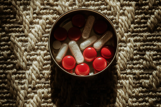 Top view of medicine box with red pills and capsules on carpet