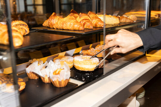 Hand picking donut with tongs in bakery display case