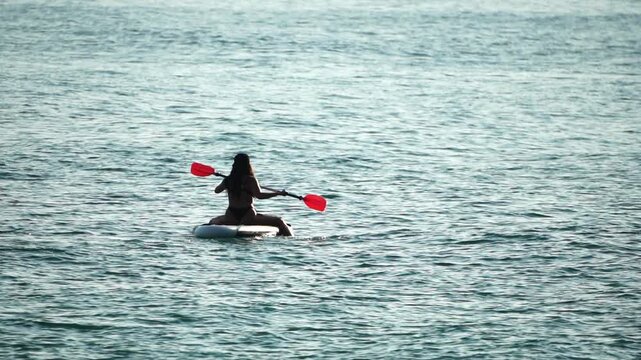 Paddleboard woman ocean paddling on a surfboard in the calm blue water during a sunny day of summer vacation