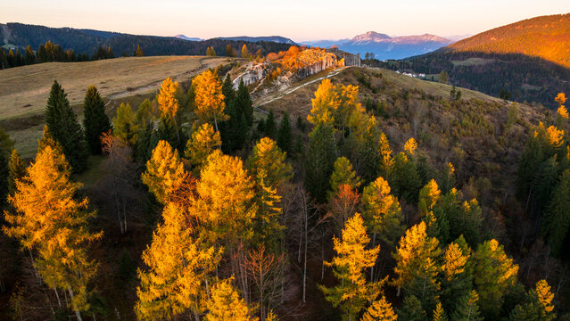 Travel, tourism: Aerial view of Cherle Fort ruins among autumn trees on a mountain ridge at sunset, Trentino, Italy. First World war.