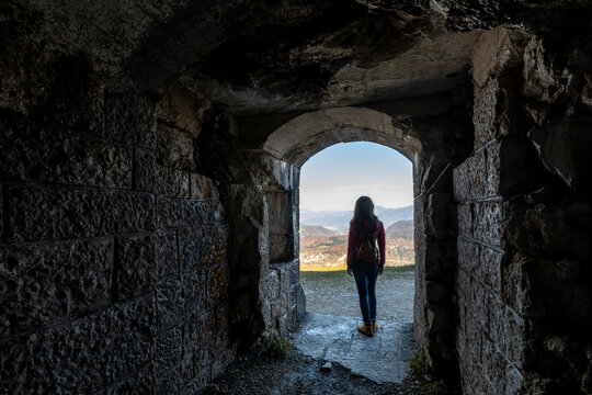Travel, tourism: Woman looks at mountain landscape from stone archway, exploring nature, freedom. First World war,Cherle Fort,Trentino,Italy.