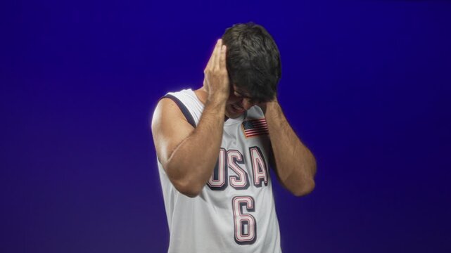 Man grimaces and covers ears with hands wearing white usa basketball jersey number 6 and american flag patch in studio; distress.