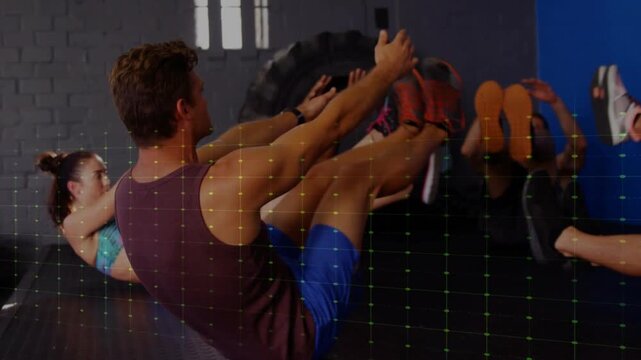 Leading man performing V-sit on gym floor, wearing maroon tank, blue shorts, with tire overlay