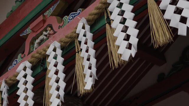 Close up shide zigzag paper and straw shimenawa rope hanging from painted shrine eave, Kyoto Japan