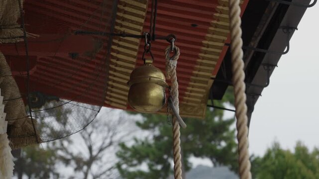 Close-up gold suzu bell and shimenawa rope hanging from red shrine ceiling, Kyoto Japan