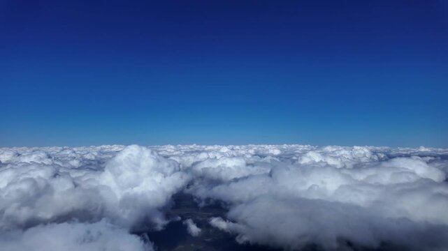 Hyperlapse taken from inside a jet cockpit flying above and into small fluffy clouds under a dep blue sky. 4K ultra-realistc shot.