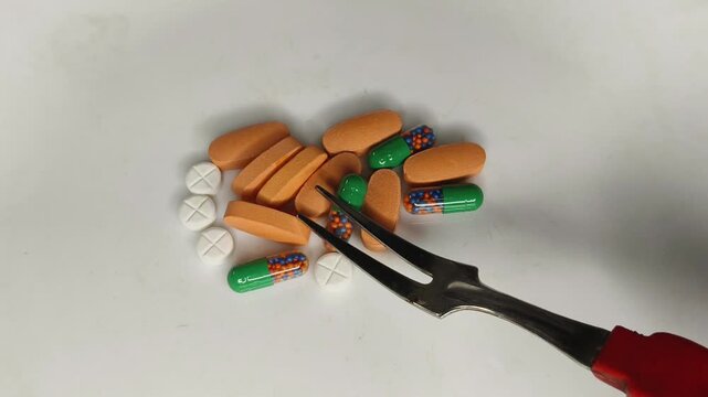 Bunch of generic medicine or drug pills, capsules and tablets isolated on white plate eating like food with fork. Unnecessary medication or supplement overuse, over consumption and addiction concept.