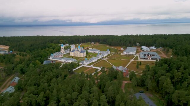 Epic remote island monastery aerial orbit. 
Cinematic 4K drone panorama of isolated 
historic christian fortress and ancient 
church inside vast northern forest.
